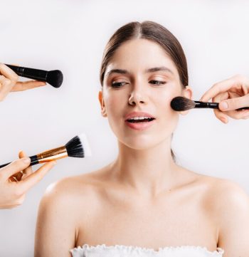 snapshot-model-with-healthy-skin-many-hands-with-makeup-brushes-reaching-out-face-young-woman_197531-13814